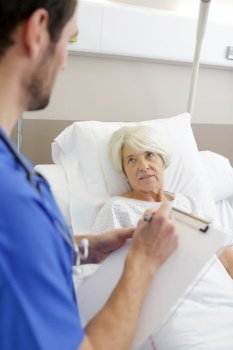 middle aged professional nurse talking to senior patient on bed
