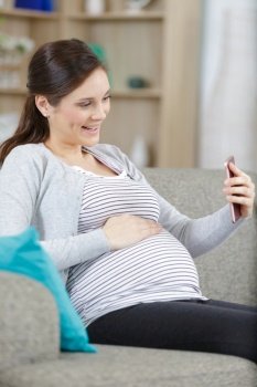 pregnant woman sitting on a couch taking a selfie