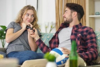 smiling young couple sharing joysticks on sofa at home
