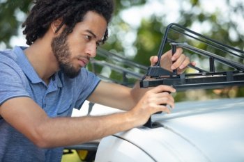 serious young man fastens roof rack on car
