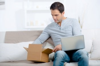young man with laptop computer opening parcel box