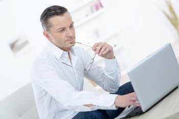 Man using laptop, holding glasses against mouth