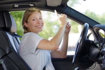 young female driver in car pointing upwards
