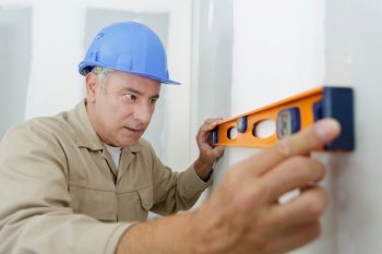 builder in uniform holding a level against the wall indoors