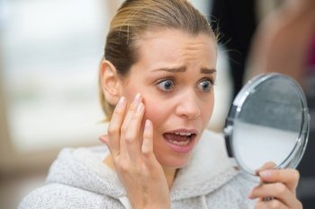 anguished young lady noticing wrinkles in the mirror