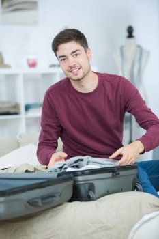 Young man packing clothes into suitcase