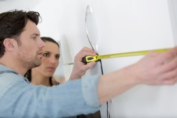 man and woman measuring the wall with a measuring tape