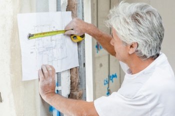 Builder using a tape measure to check building plans