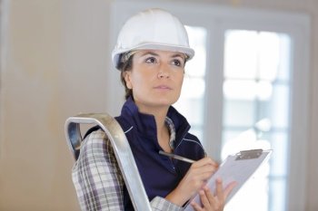 female builder inspecting site and writing on clipboard