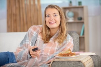 woman on sofa with fresh cake and remote watching tv