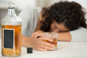 woman holding glass of whisky slumped over table