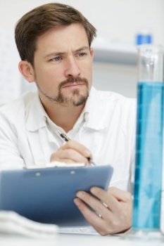 scientist looking at test tube and writing on the clipboard