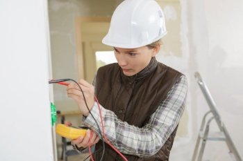 young female electrician installing electrical socket on wall
