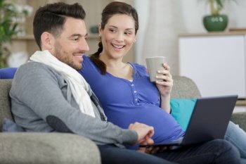 happy young pregnant and husband online shopping with laptop