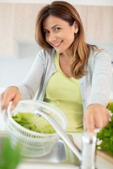 beautiful smiling woman washing lettuce in the kitchen