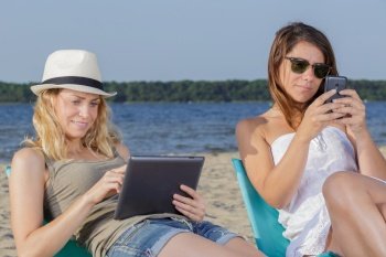 two women relaxing on the beach using tablet and smartphone