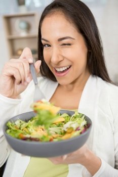 woman eating vegetable salad at table in kitchen