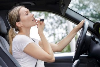 female driver applying lipstick in visor mirror