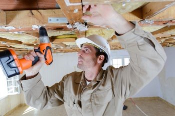 builder using cordless screwdriver on wooden ceiling joist