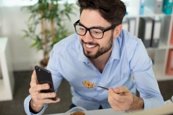 man laughing at smartphone content while eating