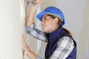 female builder removing wallpaper with scraper