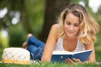 young woman sitting on the grass and reading the book