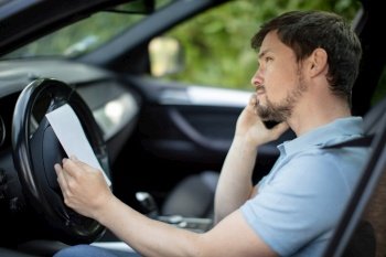 man speaking by phone in car with papers