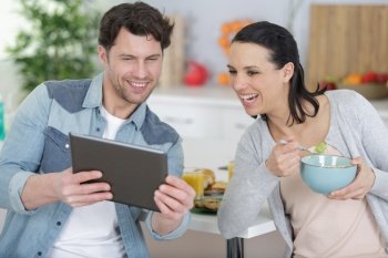 happy couple using tablet and having breakfast in the kitchen