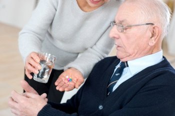 female medical assistant giving older patient pills and water