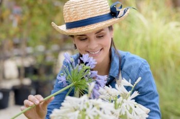 woman wearing straw hat arranges cut flowers outdoors
