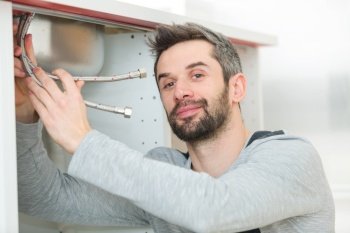 handsome plumber replacing faucet in kitchen