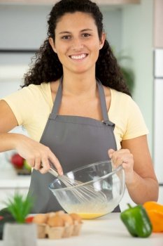 happy young woman mixing eggs in a bowl