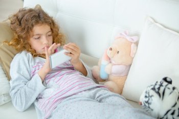 Young girl laying on sofa playing with electronic device