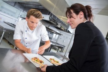 chef handing dish to waitress in kitchen