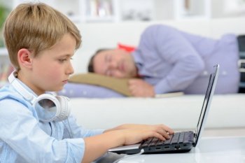 Child on laptop, father asleep on sofa