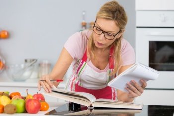 mature woman reading cookbook in the kitchen looking for recipe