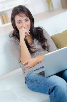 happy thoughtful woman sitting on the sofa with laptop