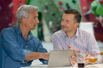 two men with drinks looking at tablet
