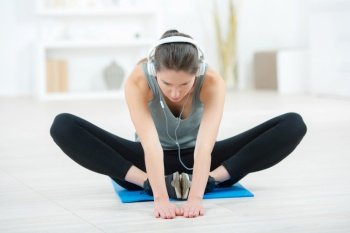young woman stretching near big windows with earphones at home