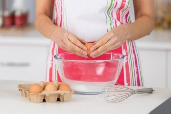 woman chef or cook breaking egg into kitchen mixing bowl