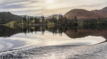 Beautiful Winter landscape image viewed from boat on Ullswater in Lake District with unusual water ripple wake movements