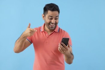 Smiling young man looking and pointing at Smartphone holding in his hand 