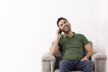 Cheerful young man talking on Smartphone while sitting on sofa