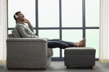 Young businessman listening music on headphone while leaning on sofa at home