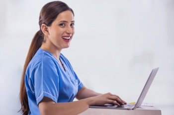 Portrait of a cheerful female nurse looking at camera while working on laptop