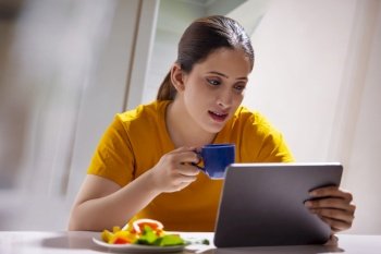 Young woman using digital laptop while drinking a cup of coffee