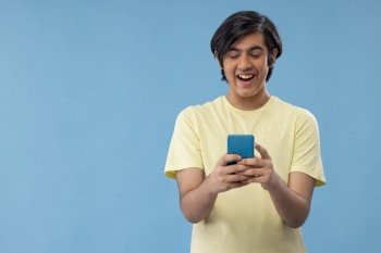 Portrait of a happy teenage boy using Smartphone while standing against blue background