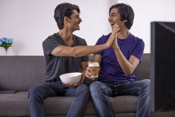 Two excited teenage boys high-fiving while watching TV in living room