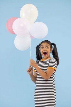 Excited girl holding colourful balloons against blue background