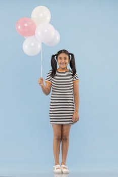 Cheerful girl holding colourful balloons against blue background